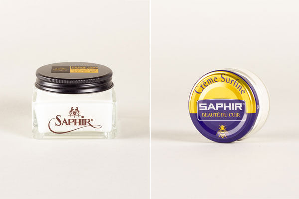 Two jars of Saphir shoe polish showcase luxury leather care, one square, one round, set against a simple background.
