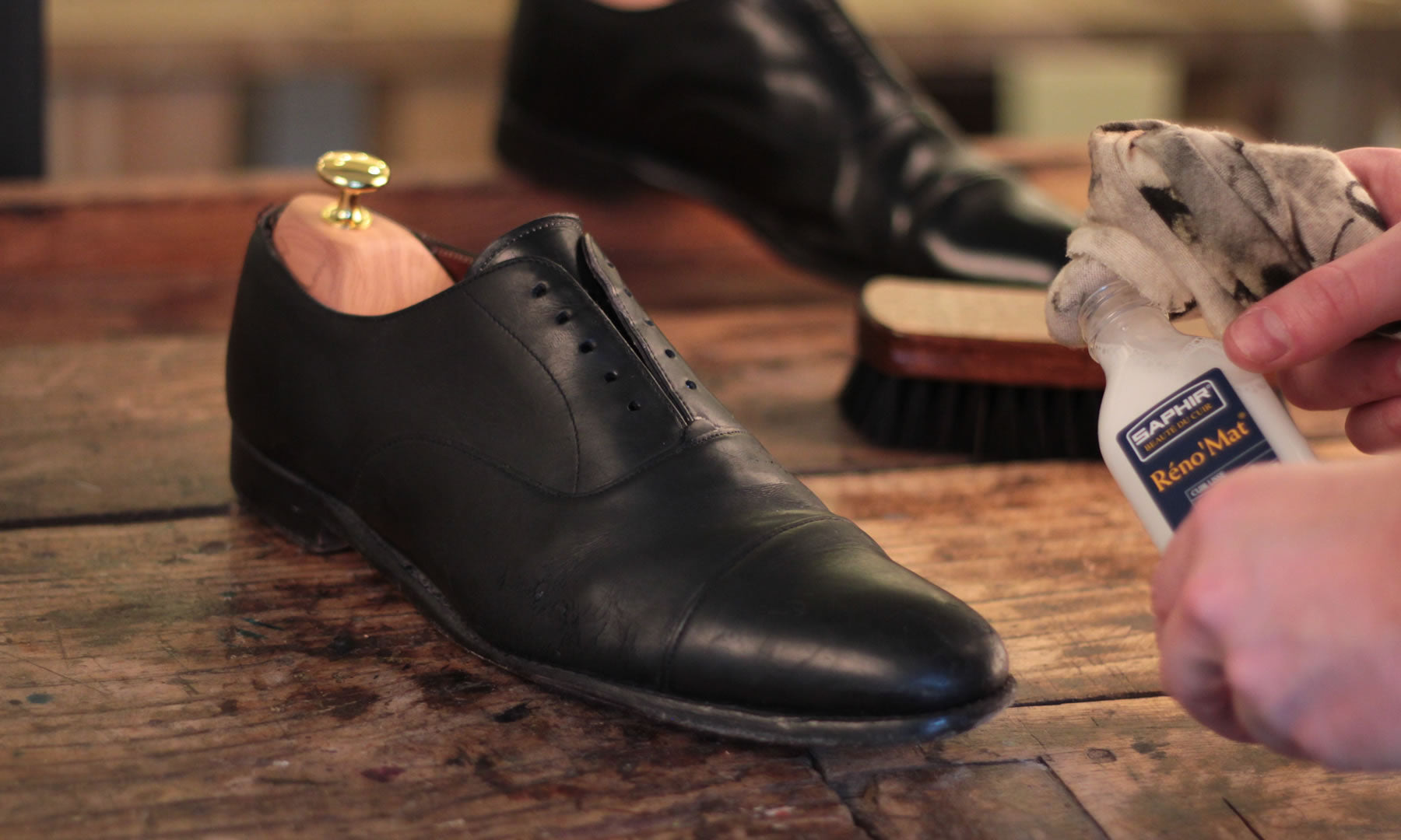 A pair of black dress shoes on a wooden table being cleaned with Saphir Réno'Mat, showcasing essential leather care.