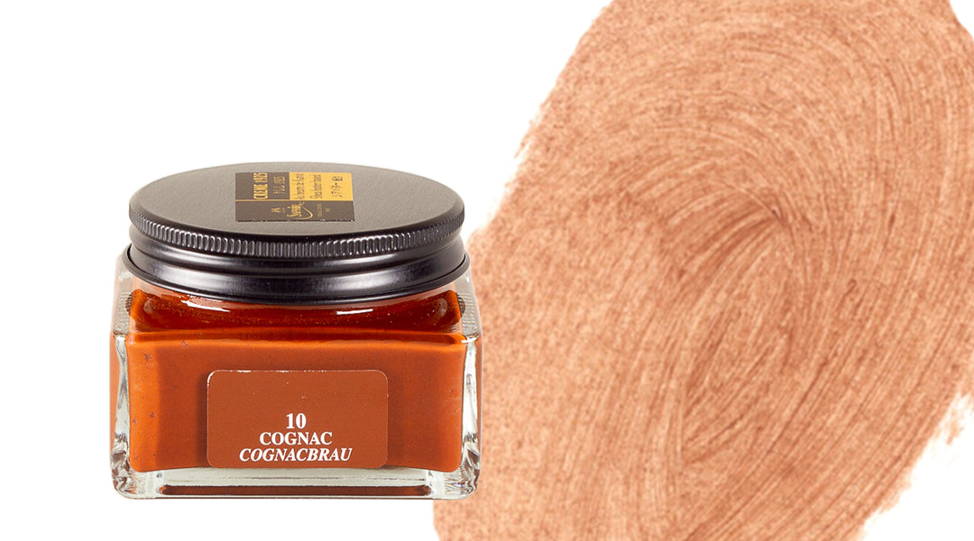 A square glass jar of brown ink labeled 10 COGNAC COGNACBRAU sits next to a large swatch of the ink in a warm, coppery-brown shade on a white background.