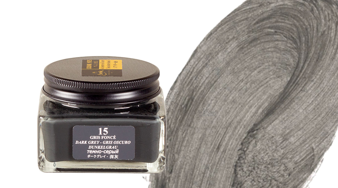 A glass jar of dark grey ink labeled “Gris Foncé 15” is shown beside a large brushstroke of the same dark grey ink color on a white background.